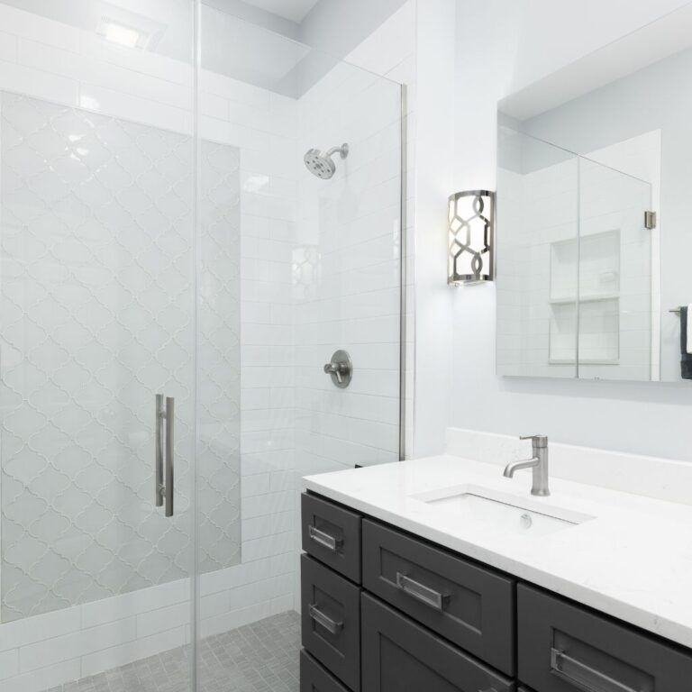 Baño en Illescas con paredes de azulejos blancos y suelo de gresite tras el cambio de bañera por plato de ducha