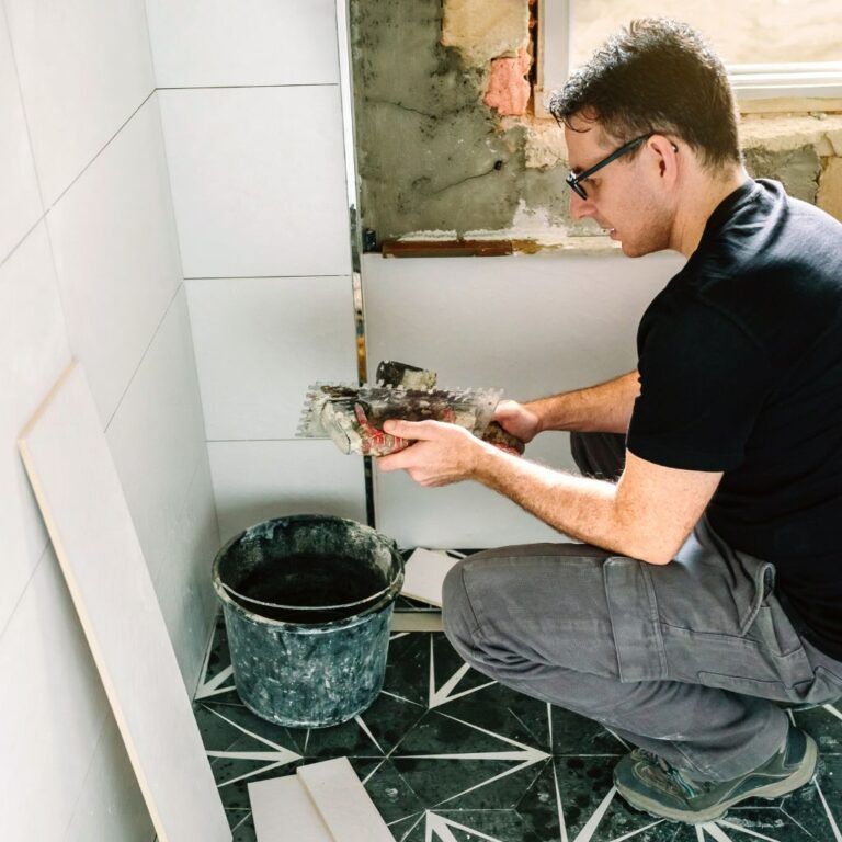 Operario instalando azulejos en un baño bajo ventana en Illescas